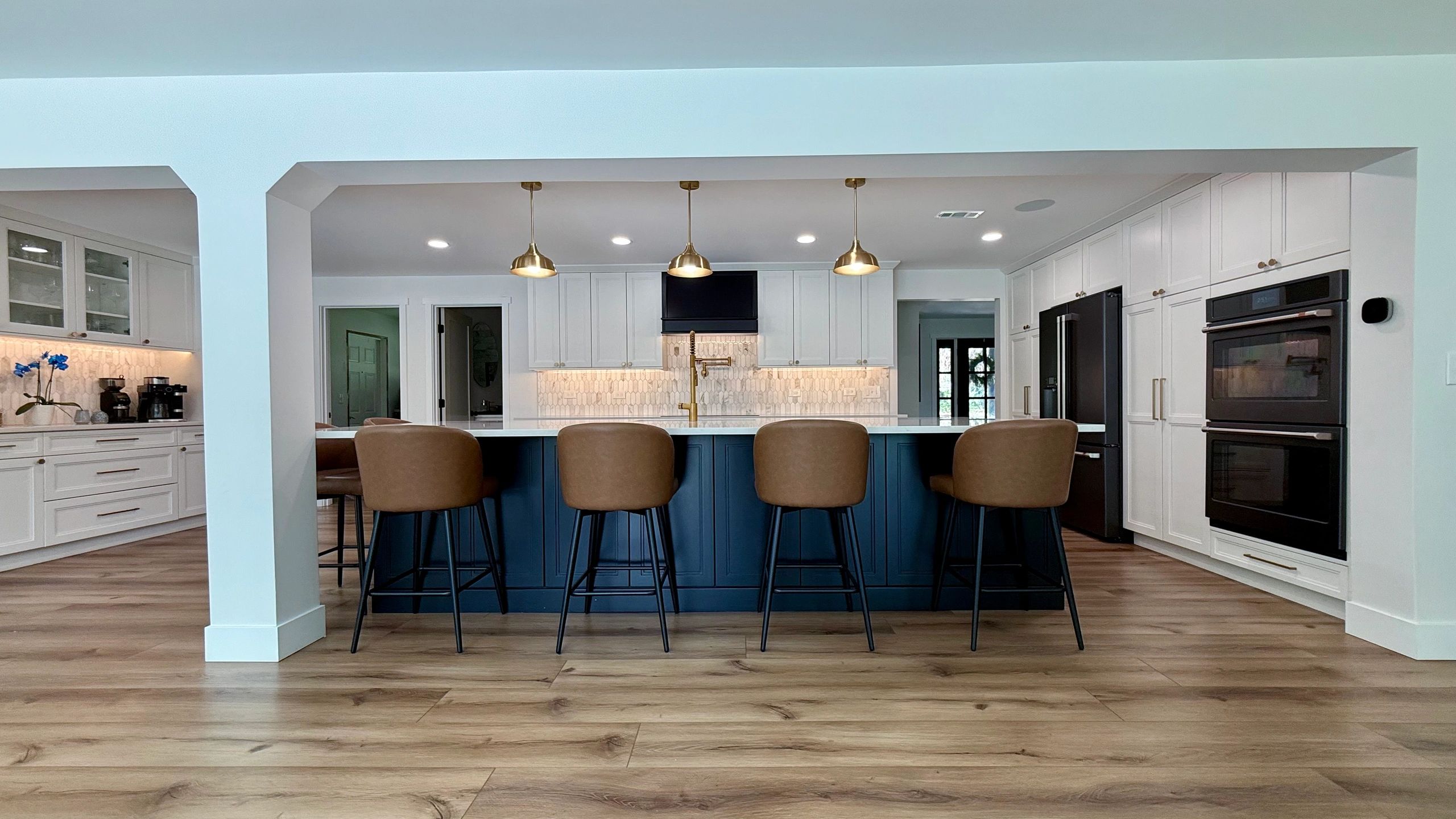 Completed kitchen with white cabinetry, blue island, and pendant lighting
